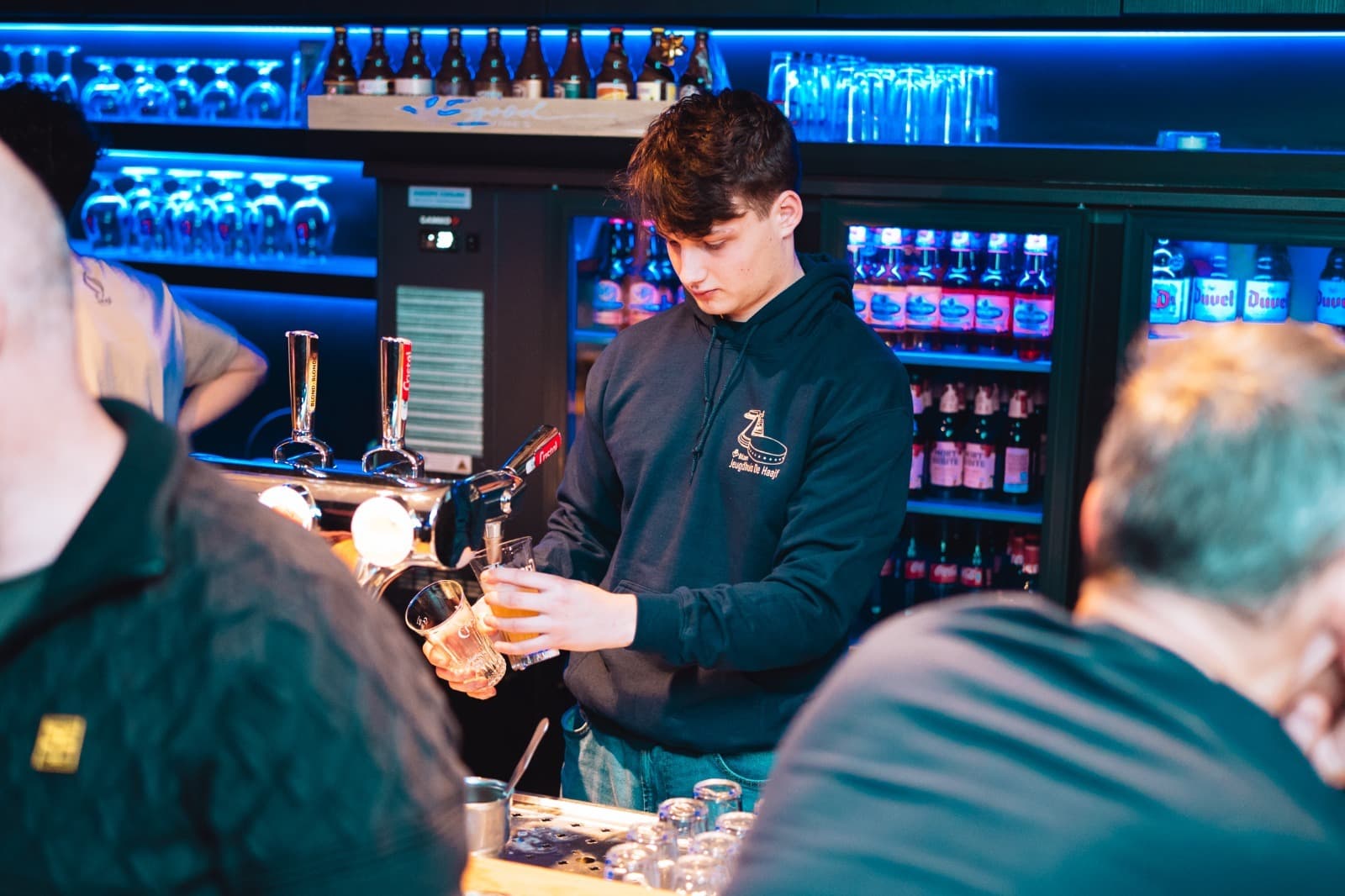 Vrijwilliger tapt een pint aan de bar van De Haajf